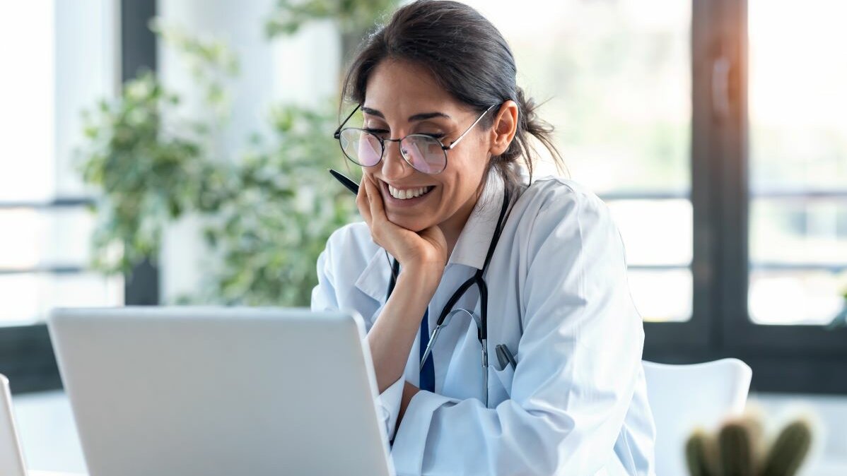 Ärztin sitzt in der Onlinesprechstunde am Laptop und hört aufmerksam zu.