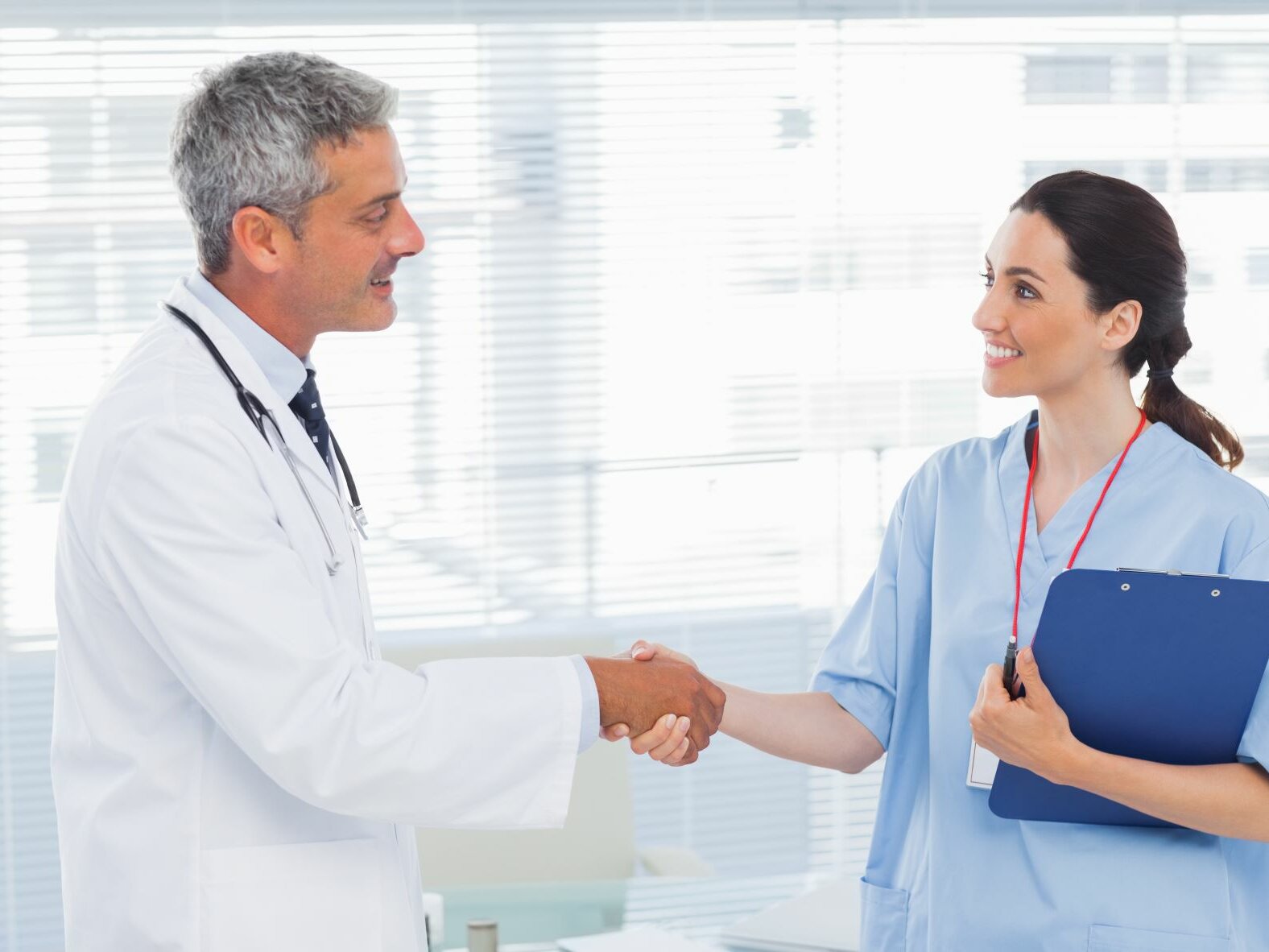Arzt schüttelt seiner Angestellten freundlich nach dem Mitarbeitergespräch die Hand