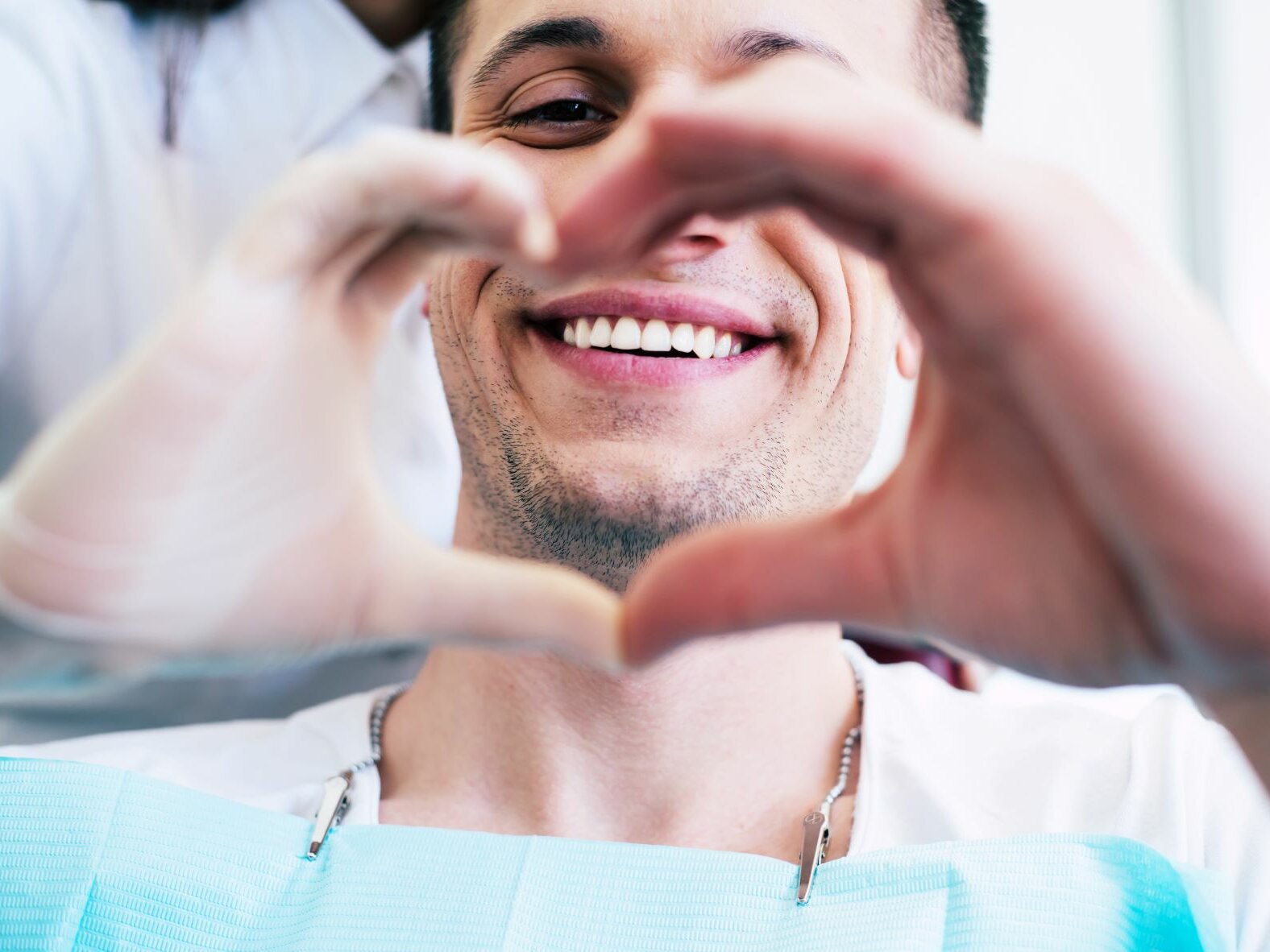 Patient auf dem Zahnarztstuhl formt mit seinen Händen ein Herz